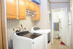 Laundry area with wallpapered walls, washing machine and dryer, light tile patterned floors, cabinet space, and a heating unit