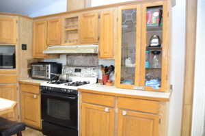 Kitchen featuring range with gas stovetop, light countertops, under cabinet range hood, stainless steel microwave, and open shelves