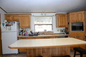 Kitchen featuring light countertops, a breakfast bar, freestanding refrigerator, a center island, and stainless steel microwave