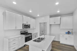 Kitchen featuring stainless steel appliances, dark wood-style floors, white cabinetry, a center island with sink, and recessed lighting