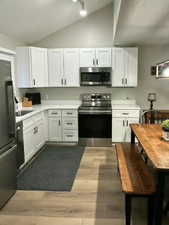 Kitchen featuring stainless steel appliances, white cabinetry, a textured ceiling, light wood-style floors, and vaulted ceiling