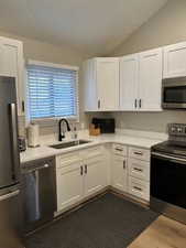 Kitchen with stainless steel appliances, white cabinetry, lofted ceiling, and light stone counters