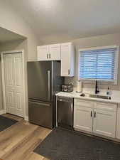 Kitchen with white cabinetry, lofted ceiling, dark wood-type flooring, a textured ceiling, and appliances with stainless steel finishes
