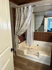 Full bath with a tub to relax in, wood finished floors, and curtained shower