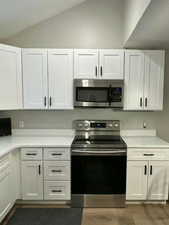 Kitchen featuring appliances with stainless steel finishes, white cabinetry, lofted ceiling, and dark wood-type flooring