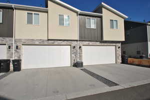 View of front facade featuring stone siding, a garage, concrete driveway, and stucco siding