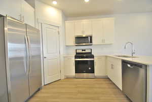 Kitchen with stainless steel appliances, light wood-style floors, a peninsula, recessed lighting, and white cabinets