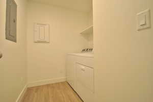 Washroom featuring light wood-style flooring, electric panel, and washer and dryer