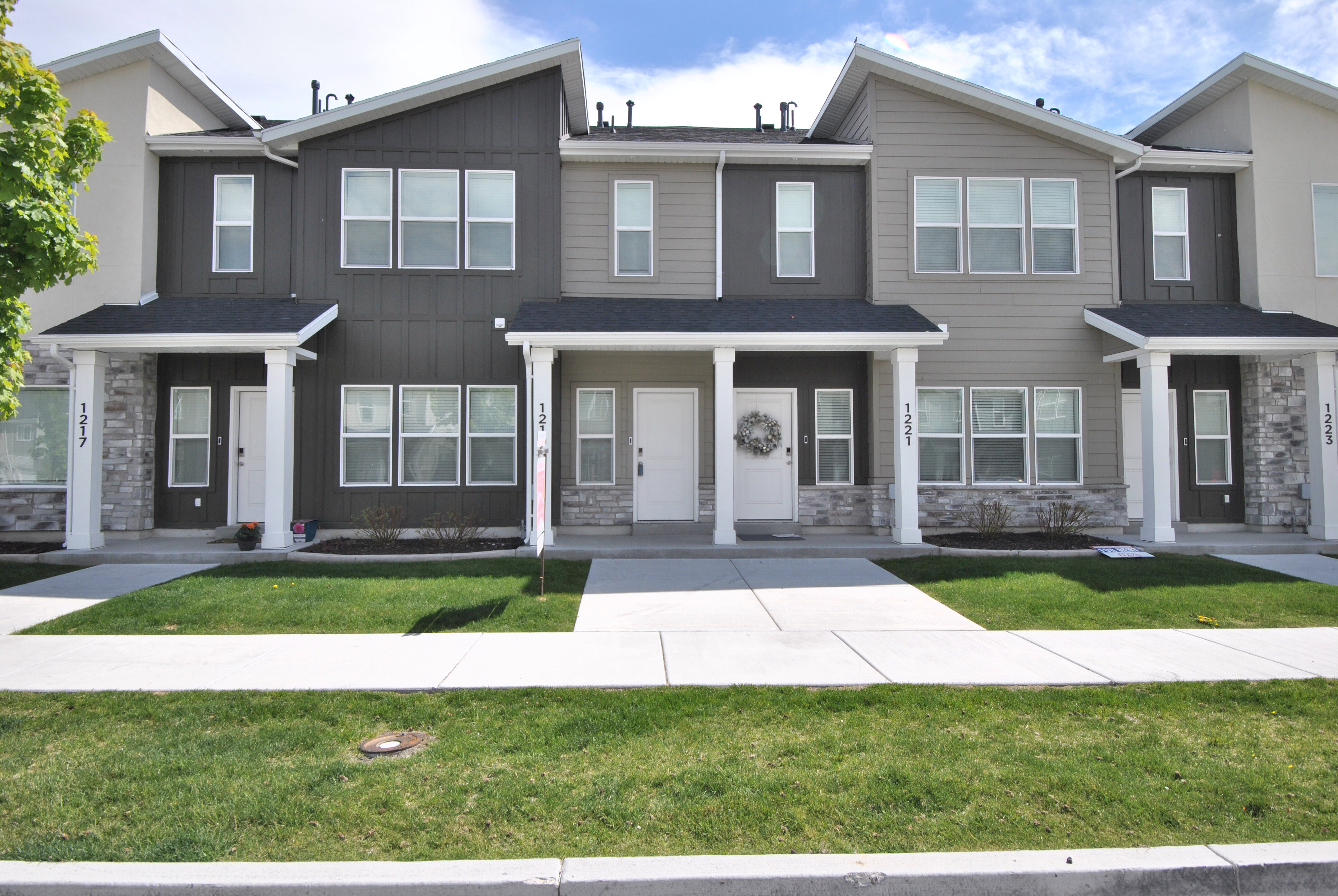Contemporary townhome facade featuring a dark gray and light gray color palette, white trim, stone veneer accents, and multiple large windows