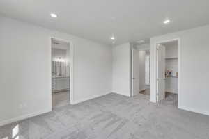 Unfurnished bedroom with a spacious closet, light colored carpet, recessed lighting, and connected bathroom