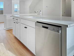 Kitchen featuring stainless steel dishwasher, light wood-style floors, an island with sink, and white cabinets