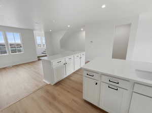 Kitchen with light wood-style floors, white cabinets, recessed lighting, open floor plan, and light stone countertops