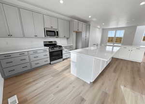 Kitchen with appliances with stainless steel finishes, a kitchen island with sink, light wood-type flooring, recessed lighting, and light stone counters