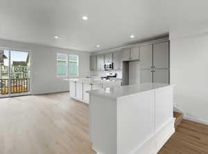 Kitchen featuring a kitchen island with sink, white range, recessed lighting, light wood-style flooring, and stainless steel microwave