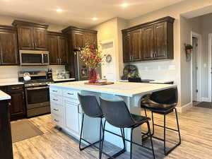 Kitchen with dark brown cabinetry, a breakfast bar, stainless steel appliances, light countertops, and recessed lighting