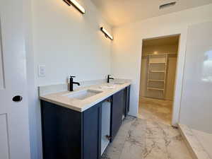 Bathroom featuring double vanity, a textured ceiling, light marble finish flooring, and a spacious closet
