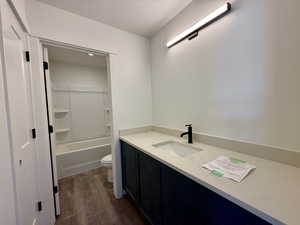 Full bath with a textured ceiling, vanity, dark wood-type flooring, and bathing tub / shower combination