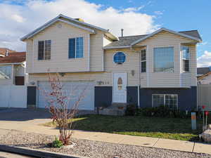 Raised ranch featuring driveway, an attached garage, brick siding, and roof with shingles