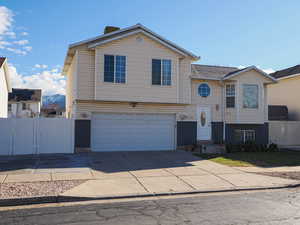 Raised ranch featuring a gate, concrete driveway, and an attached garage