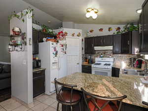 Kitchen featuring white appliances, a kitchen bar, vaulted ceiling, a peninsula, and light tile patterned floors