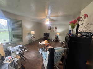 Living area featuring a textured ceiling, ceiling fan, and dark wood-type flooring