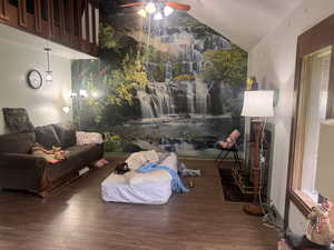 Living area with ceiling fan, wood finished floors, vaulted ceiling, and an accent wall