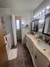 Full bath featuring a textured ceiling, double vanity, and a closet