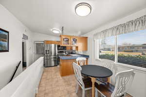 Kitchen with glass insert cabinets, appliances with stainless steel finishes, brown cabinetry, a peninsula, and dark countertops
