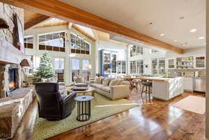 Living area featuring beamed ceiling, light wood finished floors, a stone fireplace, and high vaulted ceiling