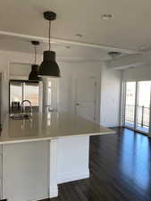 Kitchen featuring light stone countertops, dark wood finished floors, a kitchen island with sink, hanging light fixtures, and stainless steel refrigerator with ice dispenser