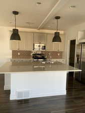 Kitchen featuring decorative backsplash, a spacious island, dark wood finished floors, stainless steel appliances, and a textured ceiling