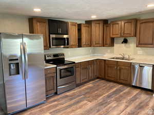 Kitchen featuring appliances with stainless steel finishes, light countertops, dark wood-type flooring, recessed lighting, and brown cabinets
