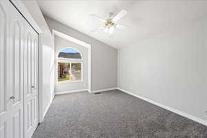 Unfurnished bedroom featuring a closet, carpet, lofted ceiling, a textured ceiling, and a ceiling fan