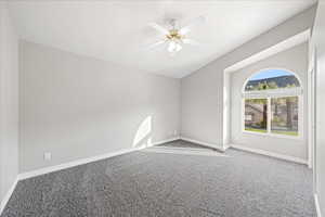 Empty room with carpet floors, lofted ceiling, ceiling fan, and a textured ceiling