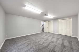 Finished basement featuring a textured ceiling, stairway, and carpet flooring