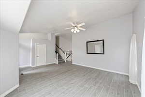 Empty room with wood tiled floors, stairway, vaulted ceiling, and ceiling fan
