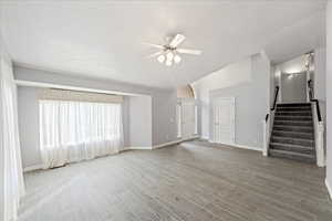 Unfurnished living room with stairs, light wood finished floors, ceiling fan, lofted ceiling, and a textured ceiling