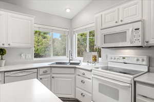 Kitchen featuring white appliances, white cabinetry, light countertops, and vaulted ceiling