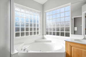 Bathroom featuring a jetted tub, vanity, and plenty of natural light