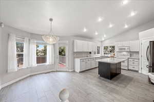 Kitchen featuring white cabinets, a center island, hanging light fixtures, stainless steel appliances, and lofted ceiling