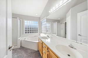 Full bath with a shower stall, vaulted ceiling, dark colored carpet, a bath, and double vanity