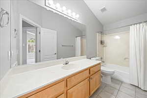Bathroom featuring vanity, shower / tub combo with curtain, lofted ceiling, and light tile patterned floors