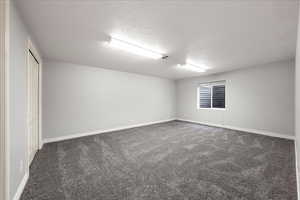 Carpeted spare room featuring a textured ceiling and baseboards