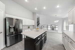 Kitchen featuring dark cabinets, white cabinets, stainless steel fridge with ice dispenser, a kitchen island, and high vaulted ceiling