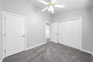 Unfurnished bedroom with dark carpet, a ceiling fan, vaulted ceiling, and a closet