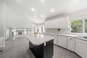 Kitchen featuring white cabinets, light countertops, white dishwasher, light wood-type flooring, and pendant lighting