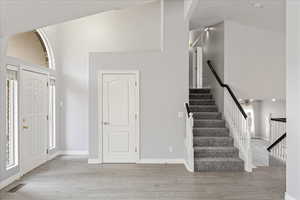 Entrance foyer with high vaulted ceiling, light wood-type flooring, and stairs