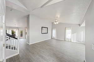Unfurnished living room with light wood finished floors, ceiling fan, stairway, a textured ceiling, and beam ceiling