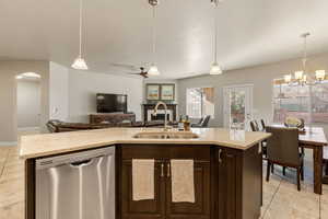 Kitchen with dark brown cabinets, stainless steel dishwasher, a center island with sink, pendant lighting, and light tile patterned floors