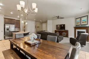 Dining room with light tile patterned flooring, a fireplace, a ceiling fan, a chandelier, and recessed lighting